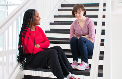 Two young adults sit on stairs together and chat with each other.
